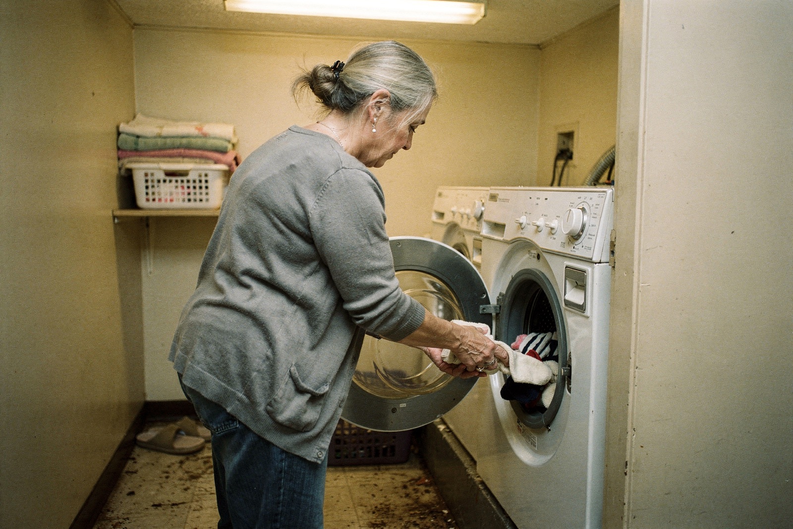 A woman in her late sixties loading socks into a washing machine in a small laundry room.